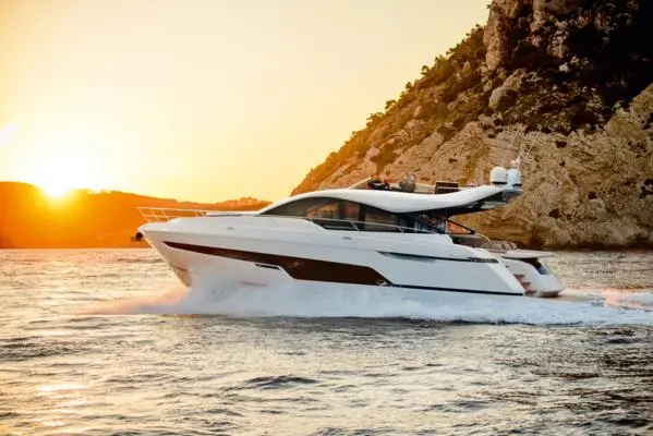Luxury yacht cruising on calm waters at sunset, surrounded by cliffs, offering a serene maritime experience.